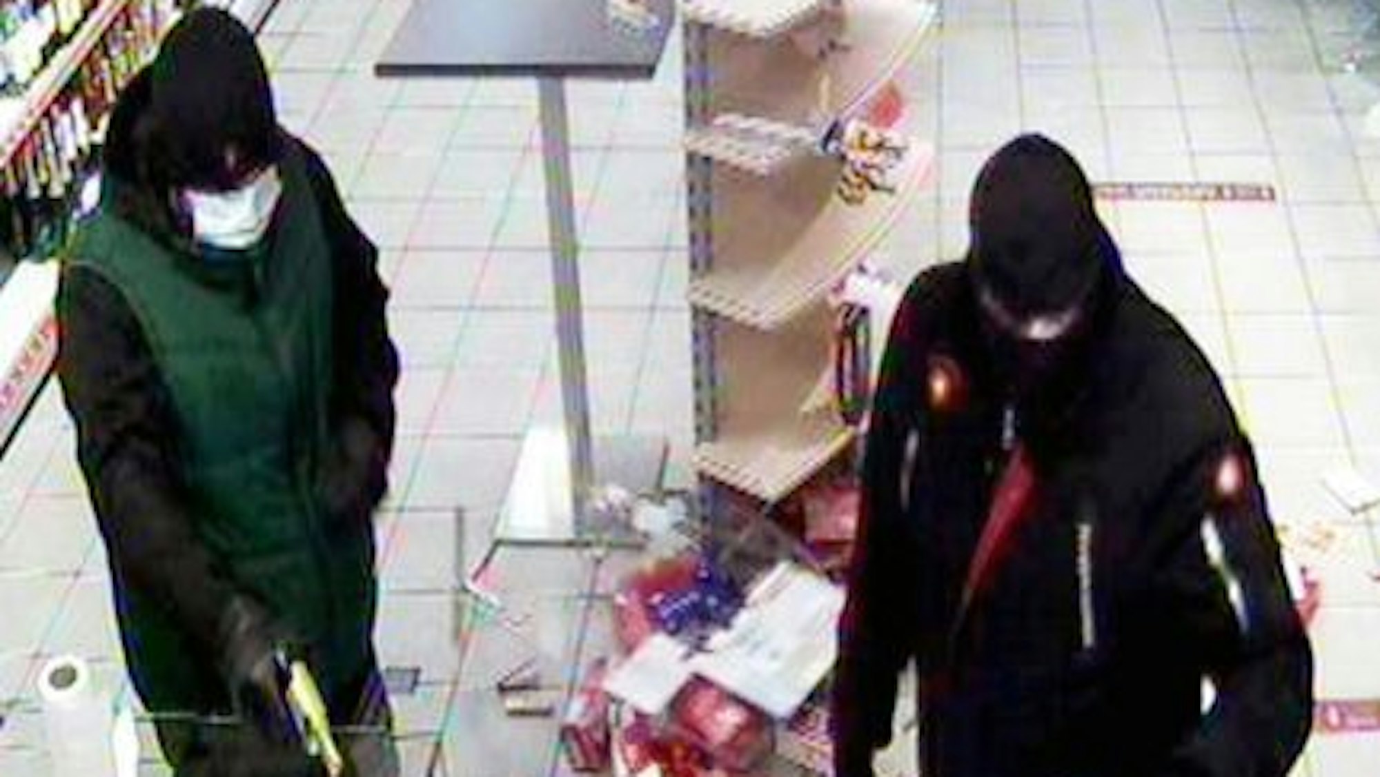 Die beiden maskierten Täter stehen vor der Kasse. Einer von ihnen hält einen Revolver.