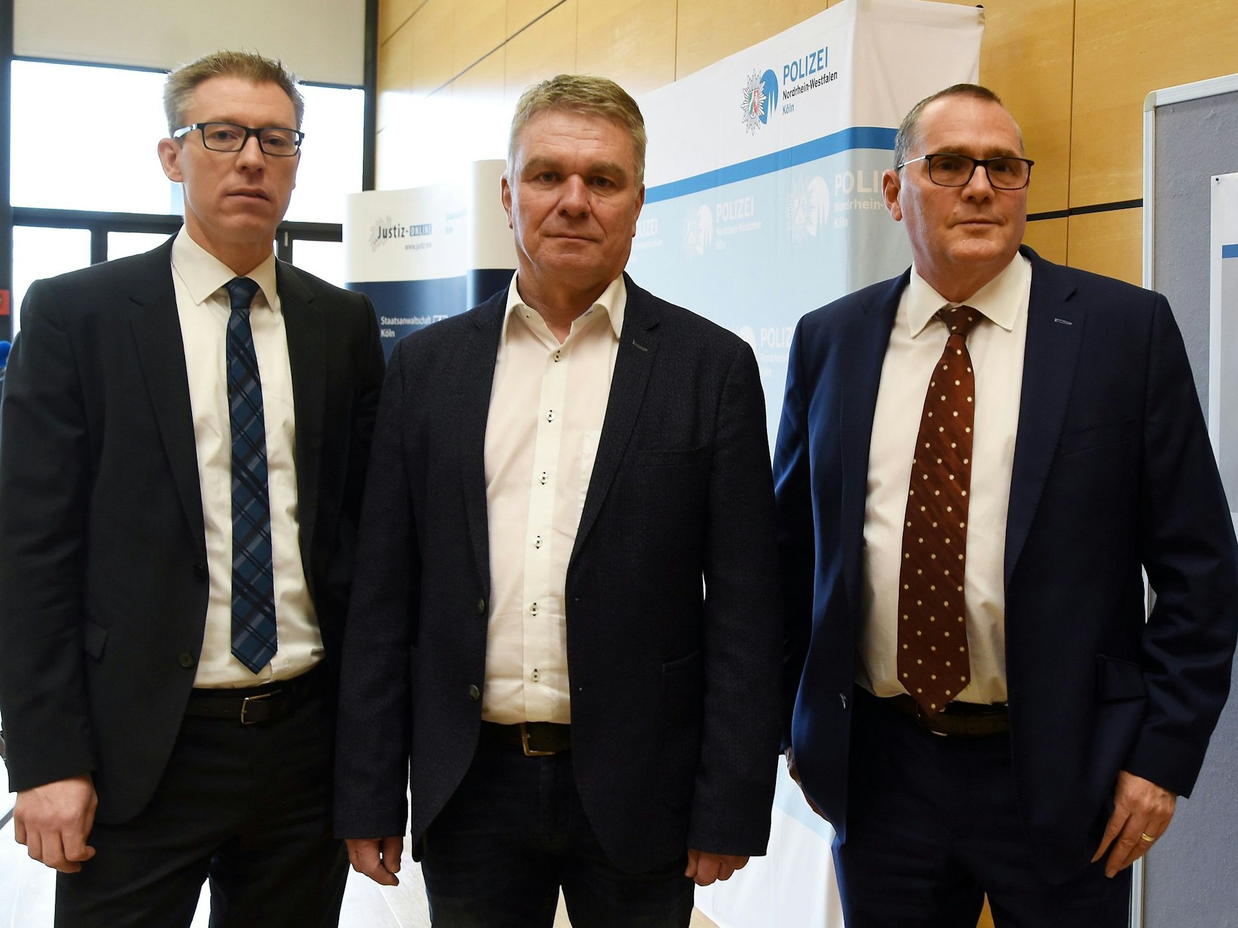 Drei Männer in Anzug stehen neben einem Plakat mit der Aufschrift Ermittlungsgruppe Cold Cases.