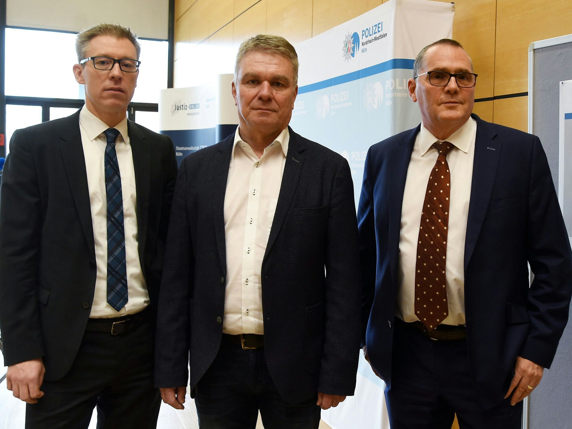 Drei Männer in Anzug stehen neben einem Plakat mit der Aufschrift Ermittlungsgruppe Cold Cases.