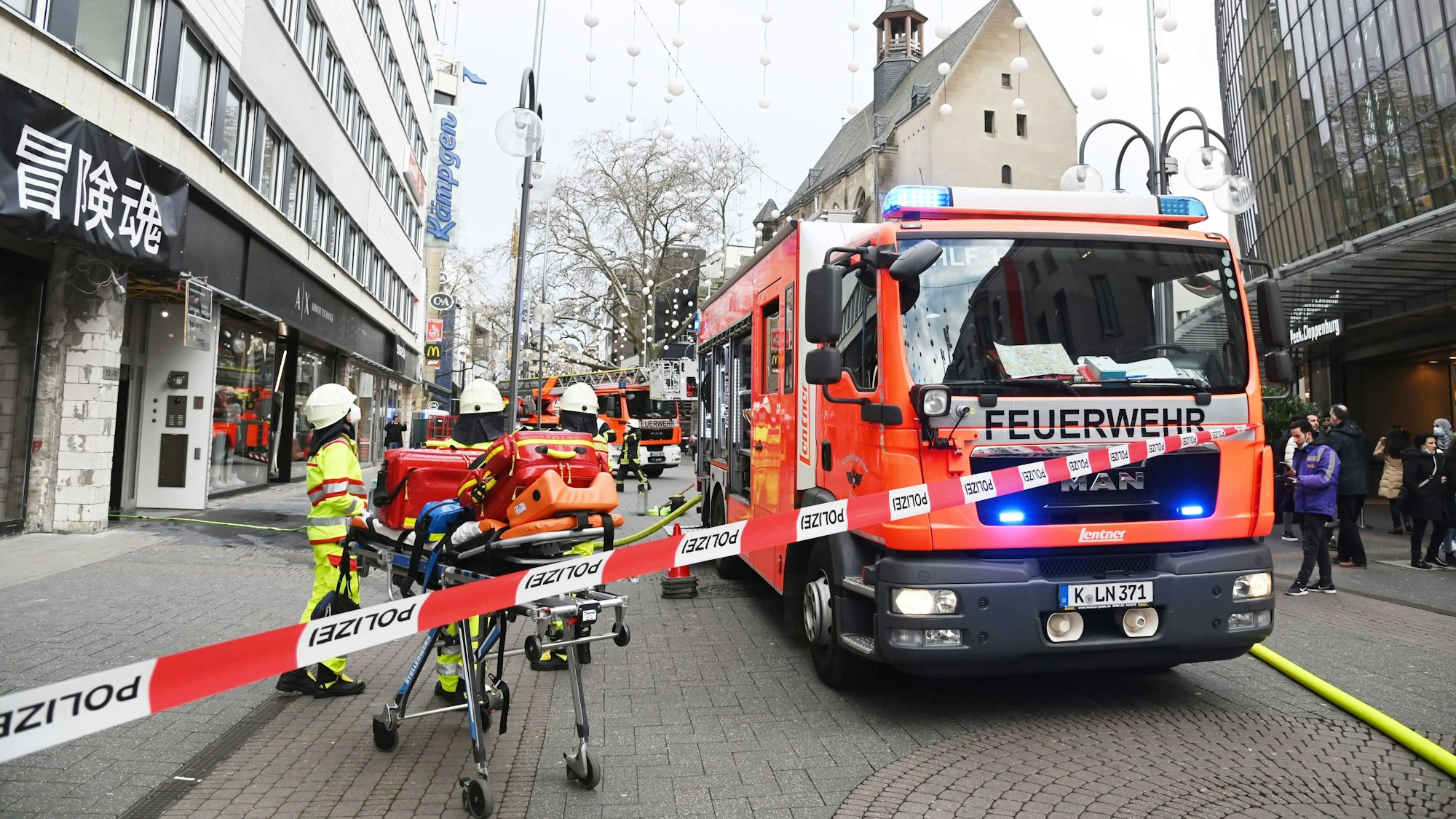 Feuerwehrfahrzeuge stehen auf der Schildergasse, der Bereich vor einem Haus ist abgesperrt, dort stehen mehrere Einsatzkräfte mit einer Trage auf Rollen.