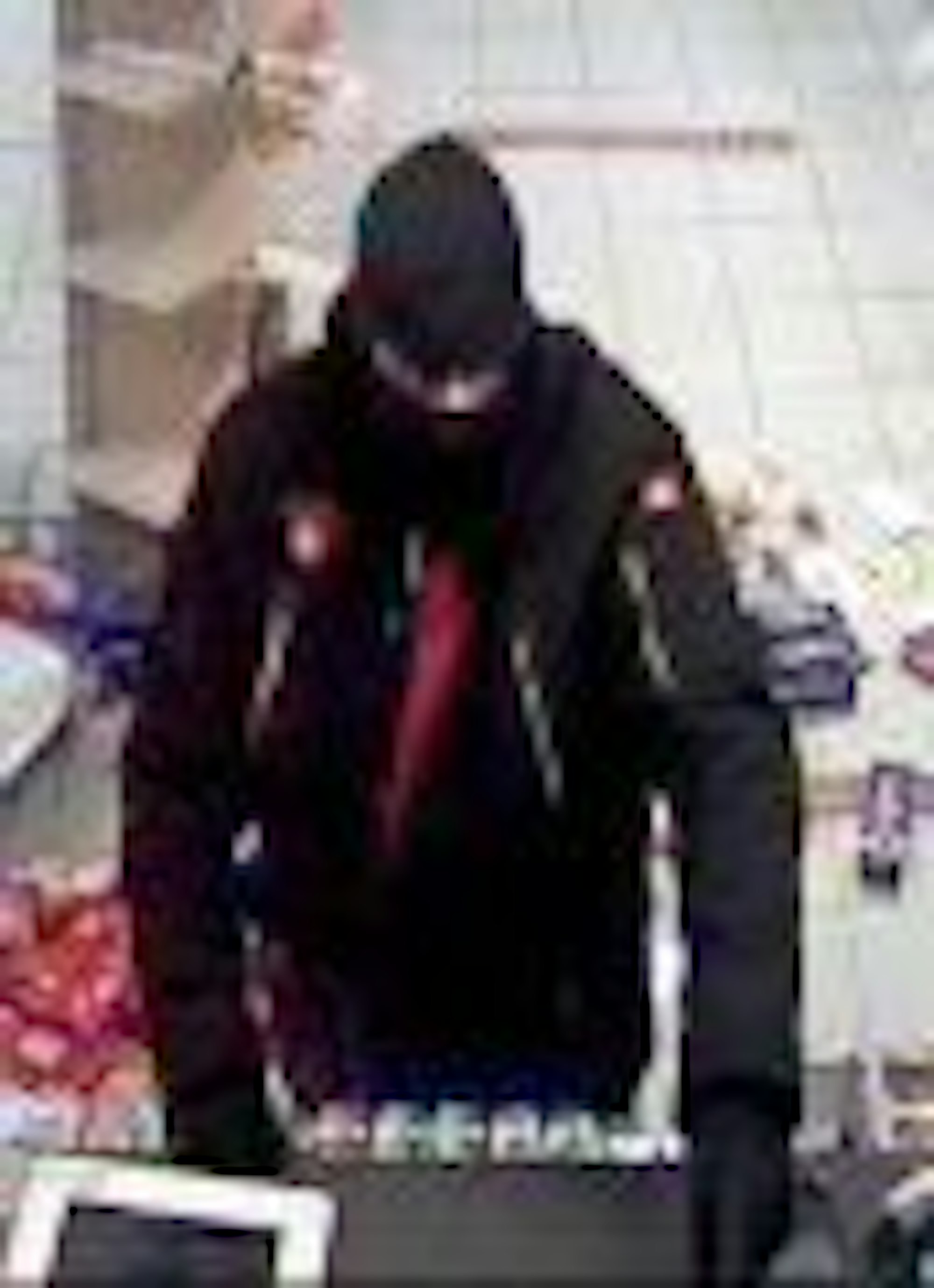 Der Komplize des Revolver-Täters steht vor der Kasse und ist dunkel gekleidet.