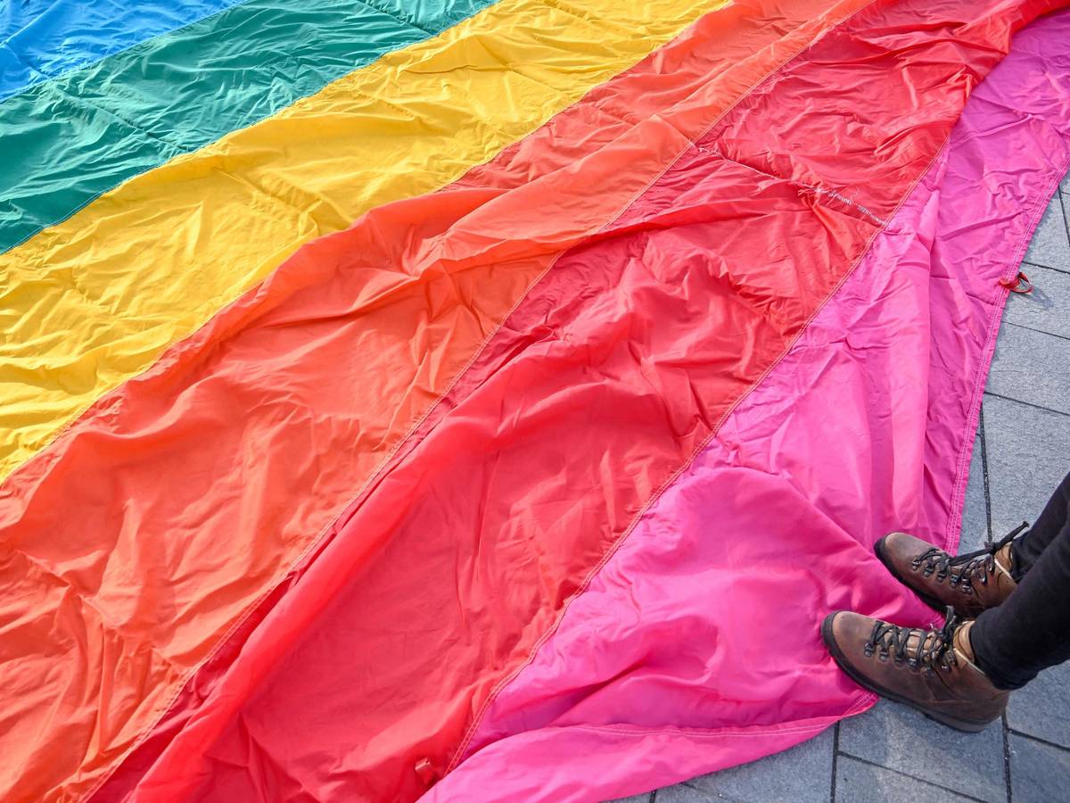 Auf dem Boden liegt eine große LGBTQI+-Flagge und jemand steht darauf.