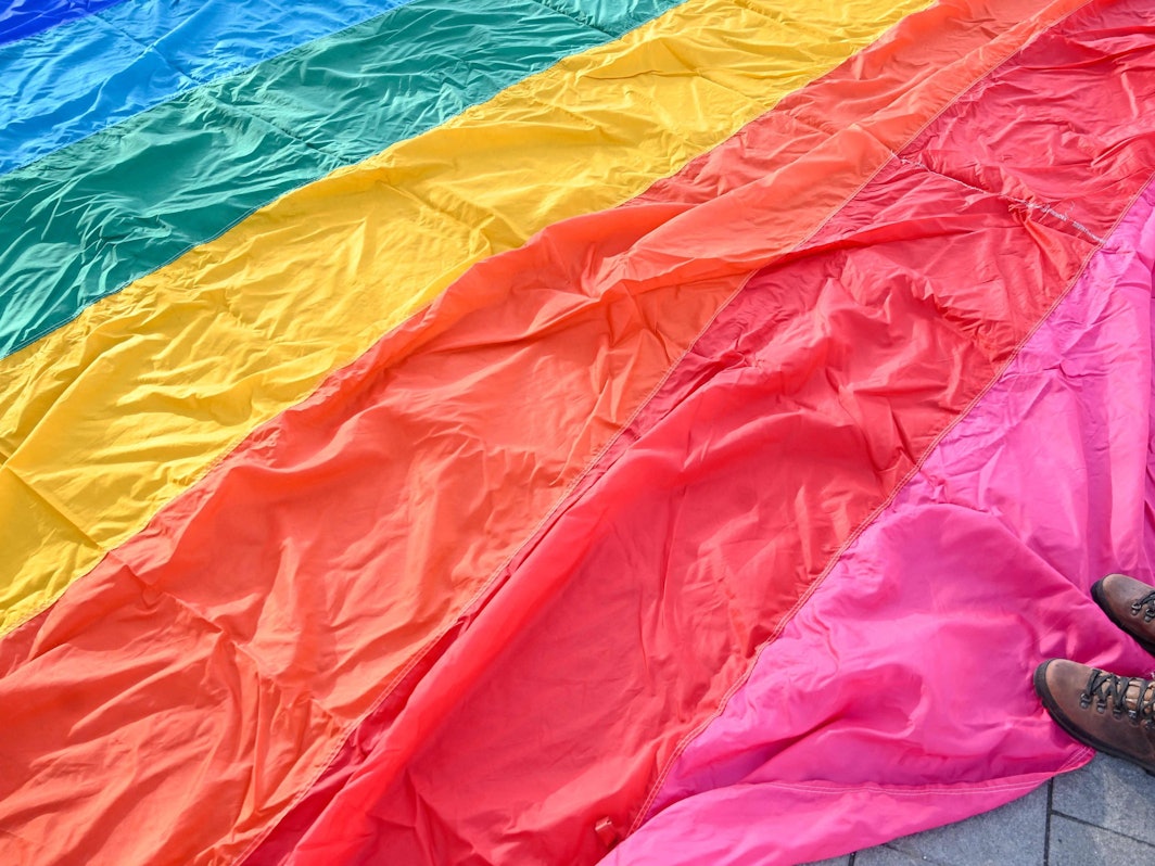 Auf dem Boden liegt eine große LGBTQI+-Flagge und jemand steht darauf.