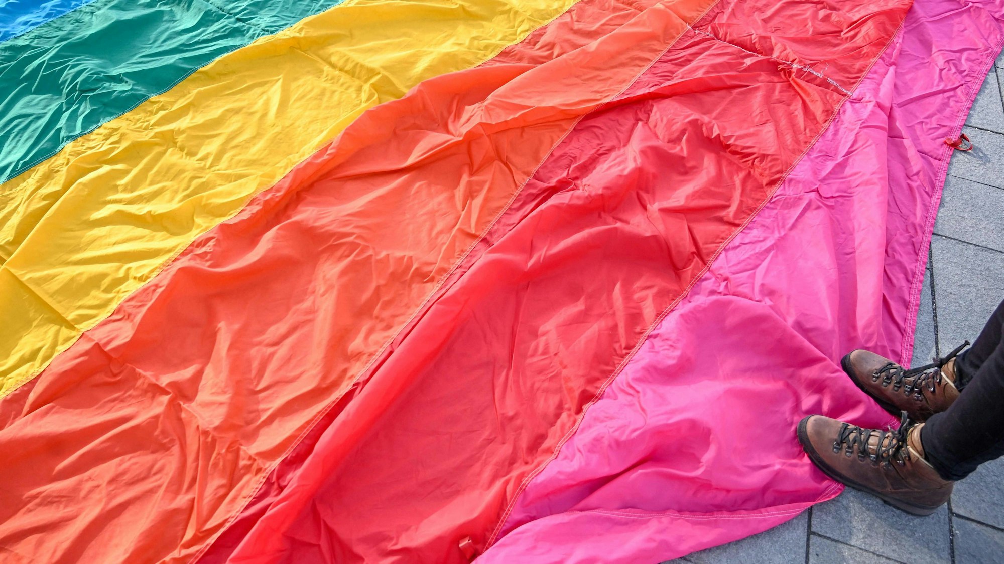 Auf dem Boden liegt eine große LGBTQI+-Flagge und jemand steht darauf.