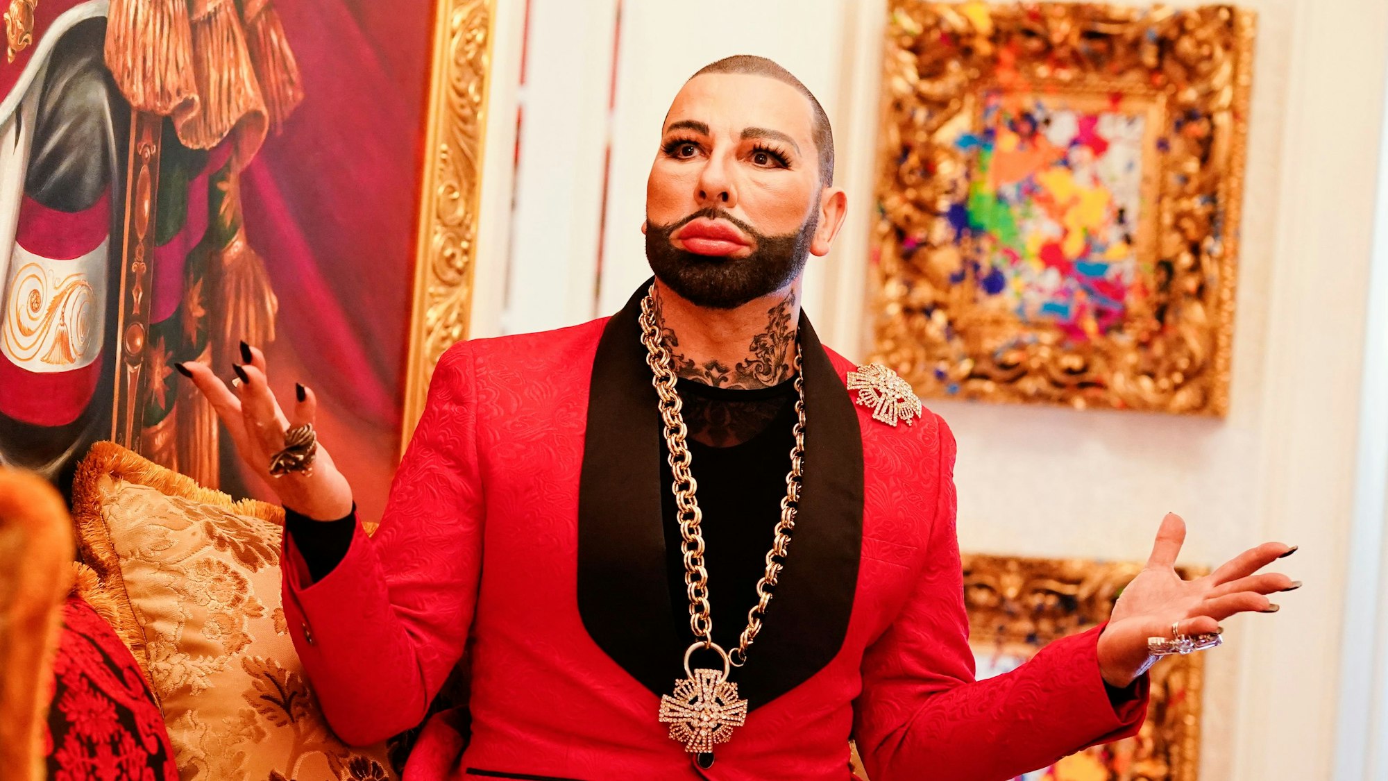 Harald Glööckler sitzt auf einem pompösen Sofa.