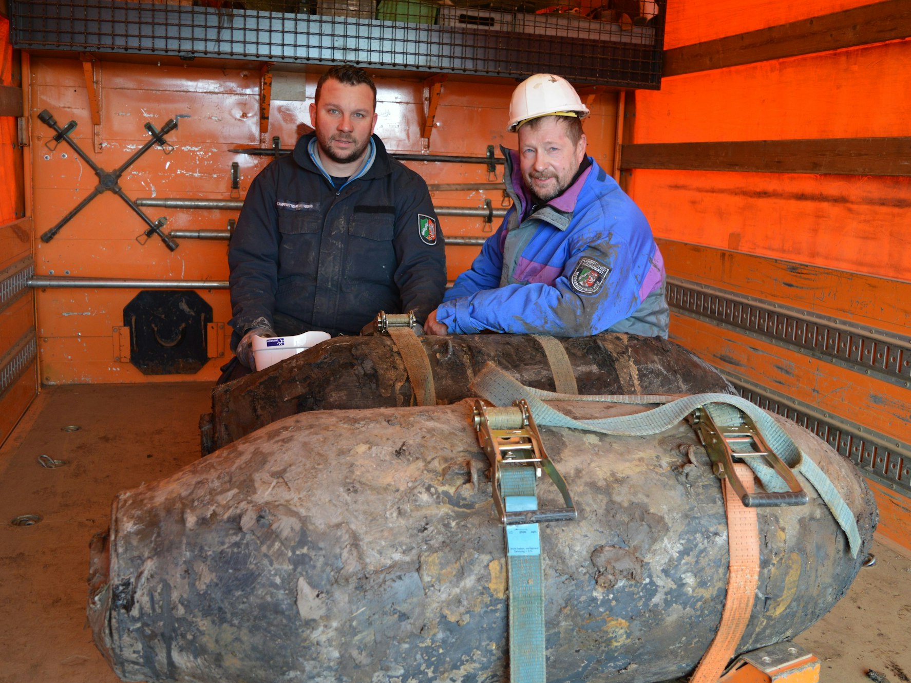 Zwei Männer posieren mit zwei Weltkriegsbomben.