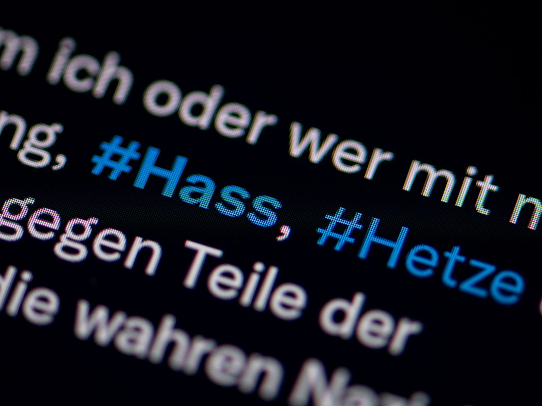 Auf dem Bildschirm eines Smartphones sieht man die Hashtags Hass und Hetze in einem Twitter-Post.