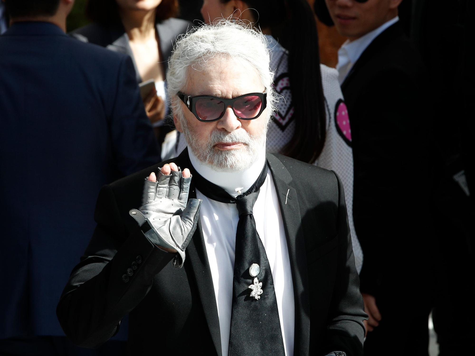 Karl Lagerfeld winkt auf der Paris Fashion Week 2018 in die Kamera.