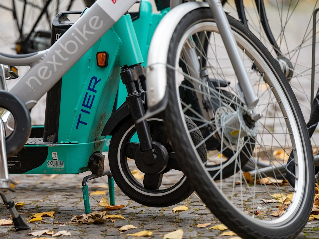 E-Tretroller des Anbieters Tier und ein Leihfahrrad von Nextbike stehen nebeneinander auf einem Gehweg.