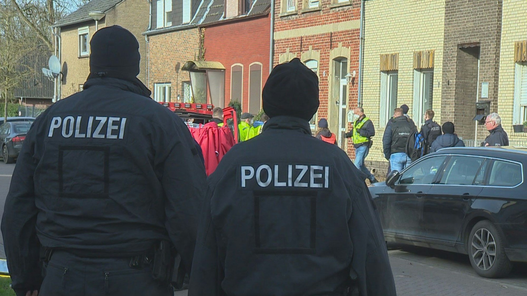 Einsatzkräfte der Polizei stehen bei einer Razzia vor einem Haus.