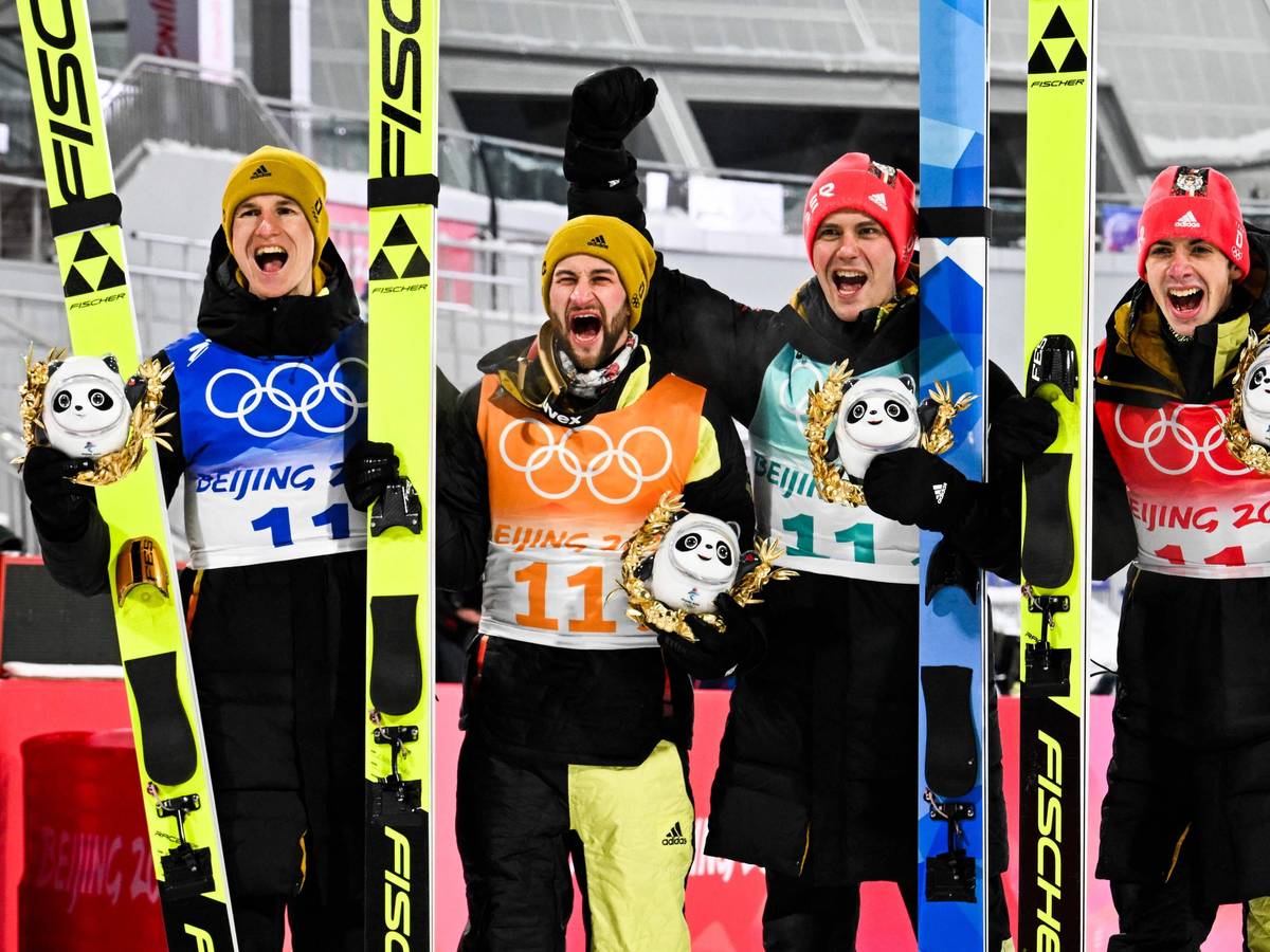 Die deutschen Skispringer Constantin Schmid, Stephan Leyhe, Markus Eisenbichler und Karl Geiger jubelnd auf dem Podium nach dem Gewinn der Bronzemedaille im Team am 14. Februar 2022.