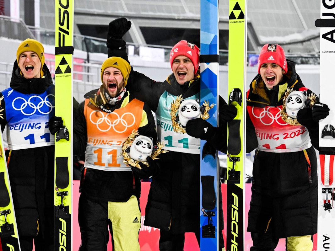 Die deutschen Skispringer Constantin Schmid, Stephan Leyhe, Markus Eisenbichler und Karl Geiger jubelnd auf dem Podium nach dem Gewinn der Bronzemedaille im Team am 14. Februar 2022.