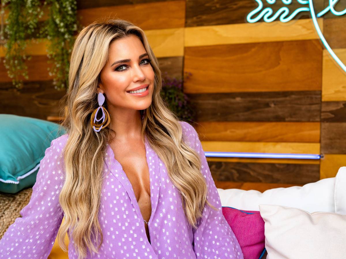 Sylvie Meis während Aufnahmen für den "Love Island"-Podcast. Das Foto zeigt die Moderatorin lächeln auf einer Couch vor einer Holzwand.