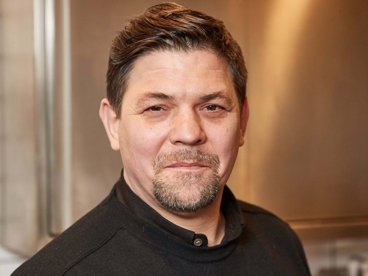 Fernsehkoch Tim Mälzer steht in der Küche seines Restaurants ««Die Gute Botschaft»». Dabei lächelt er leicht in die Kamera.