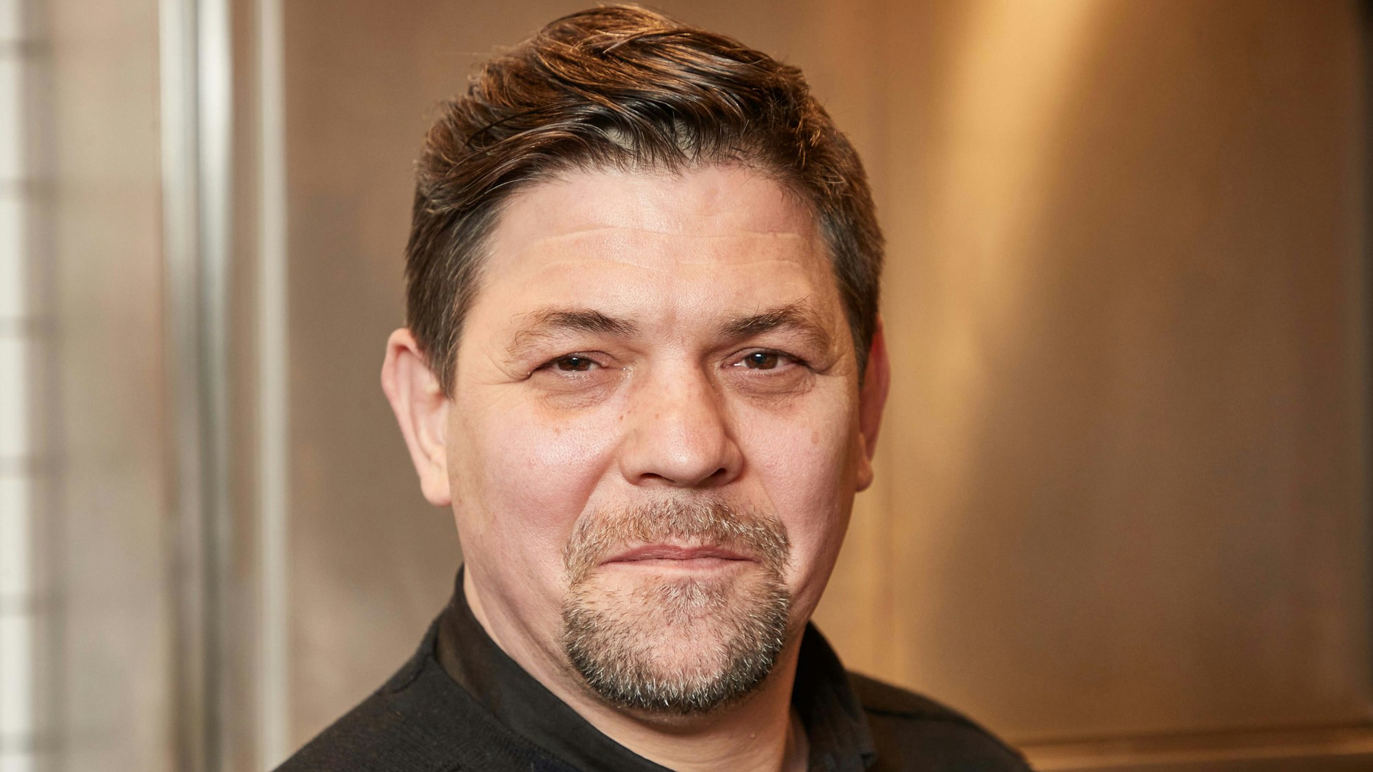 Fernsehkoch Tim Mälzer steht in der Küche seines Restaurants ««Die Gute Botschaft»». Dabei lächelt er leicht in die Kamera.