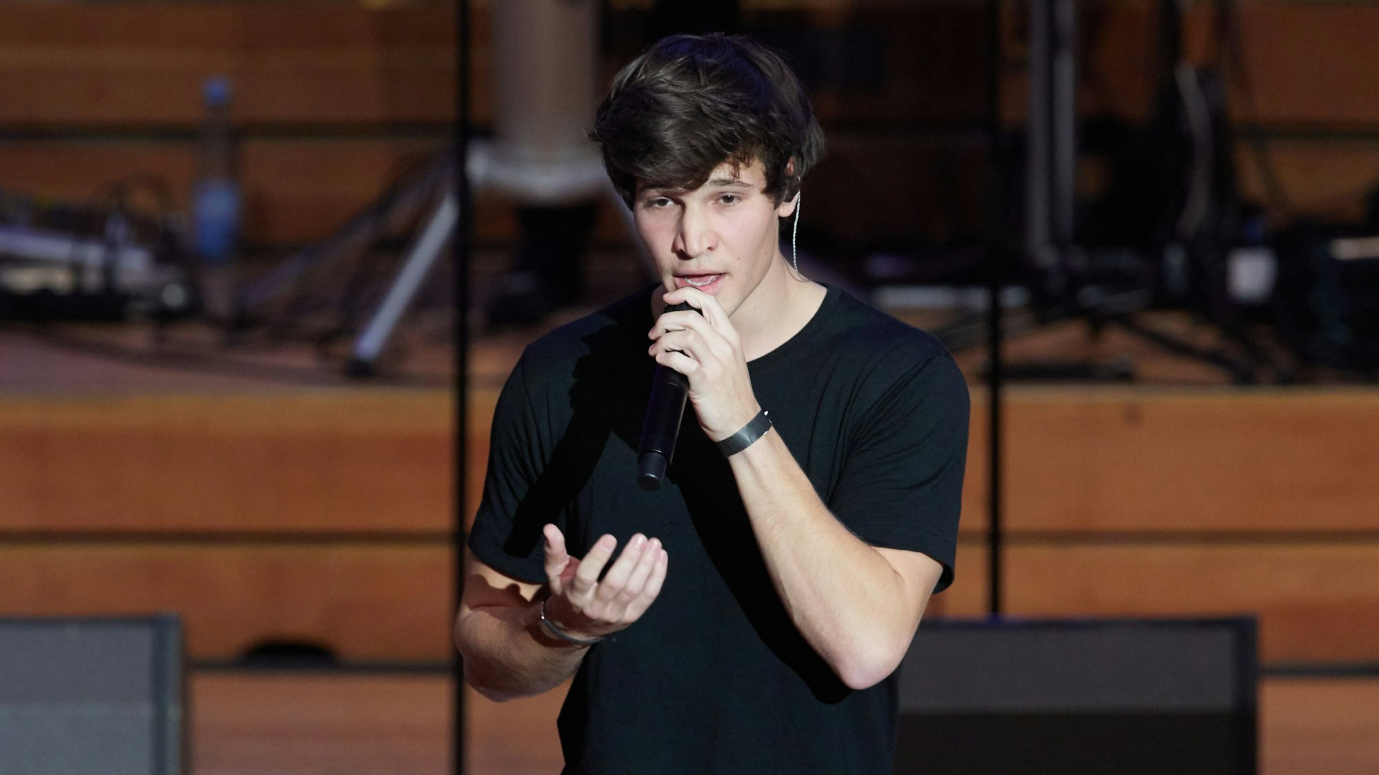 Wincent Weiss, Pop-Sänger, steht zum weltweit ersten Facebook-Weihnachtskonzert auf der Bühne in der Laeiszhalle. Dabei hält er sich ein Mikrofon vor den Mund und gestikuliert mit der rechten Hand.