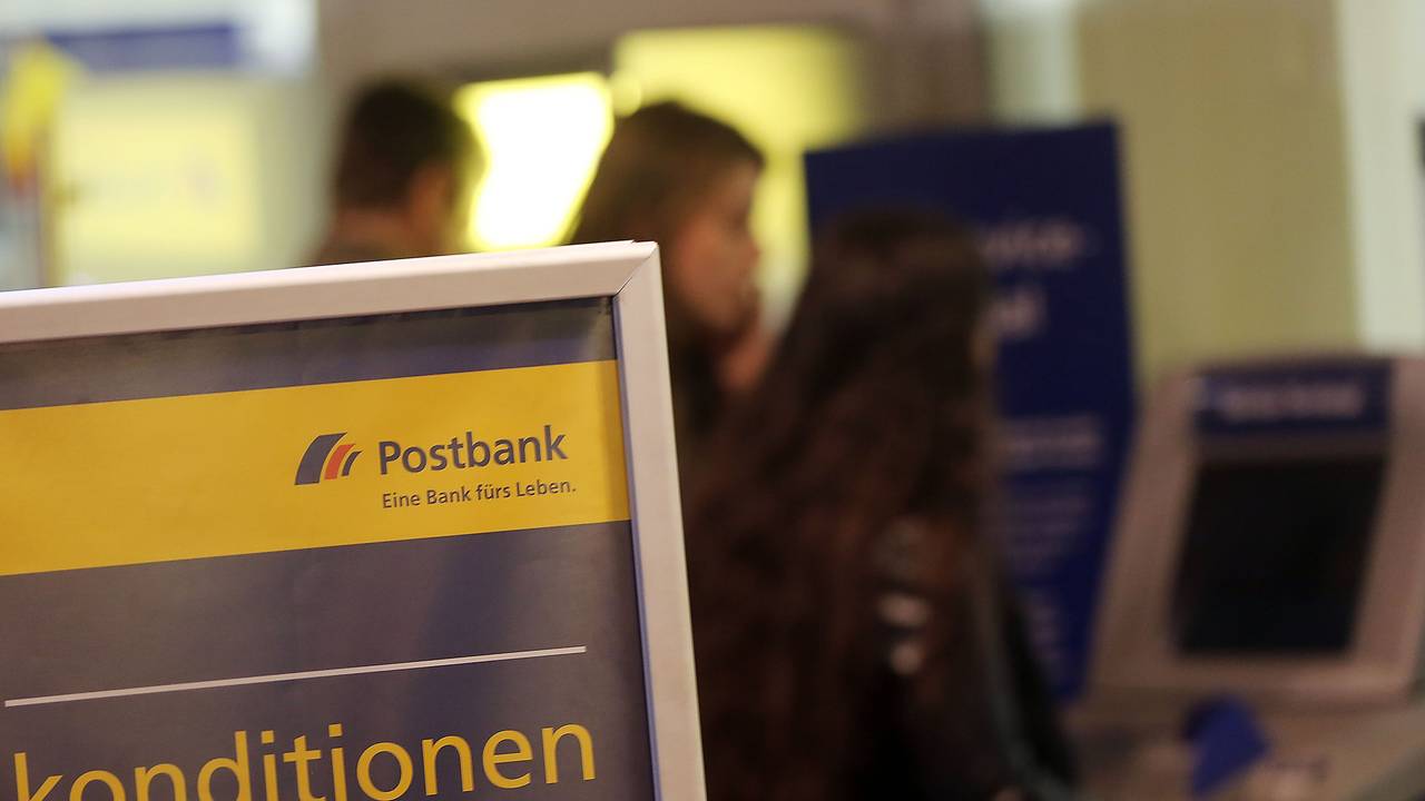 Kunden und Kundinnen der Postbank stehen am 27. Januar 2015 in Köln (Nordrhein-Westfalen) vor einer Filiale am Geldautomaten.