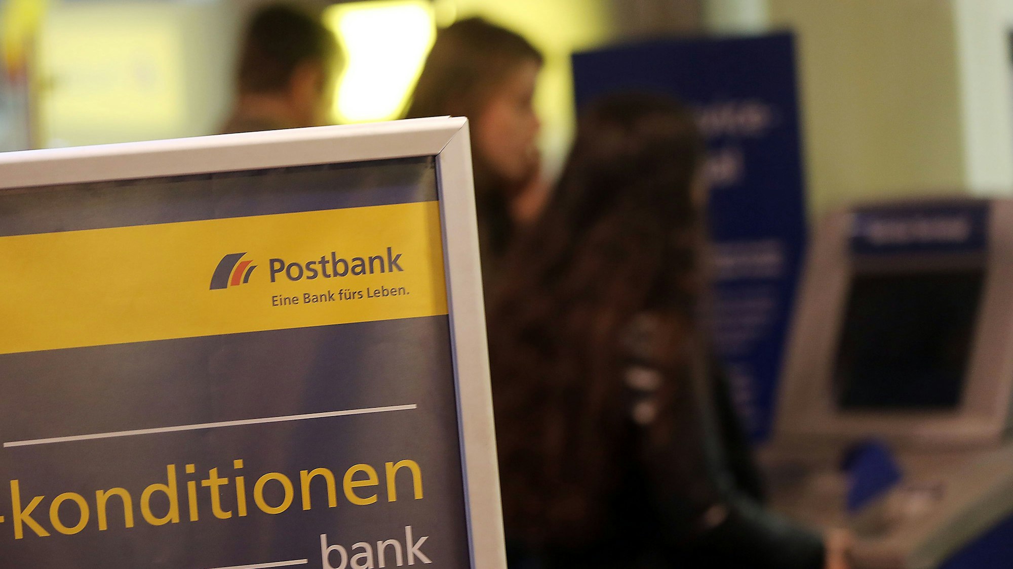 Kunden und Kundinnen der Postbank stehen am 27. Januar 2015 in Köln (Nordrhein-Westfalen) vor einer Filiale am Geldautomaten.