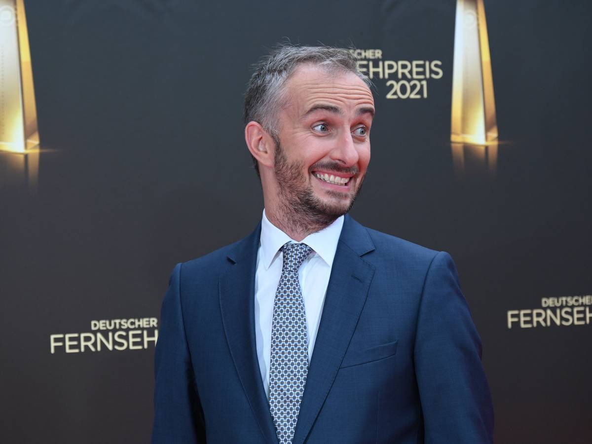 Jan Böhmermann kommt zur Verleihung des Deutschen Fernsehpreises 2021 im Tanzbrunnen. Der Satiriker steht vor einer Wand mit dem Logo der Veranstaltung und grinst schief an der Kamera vorbei.