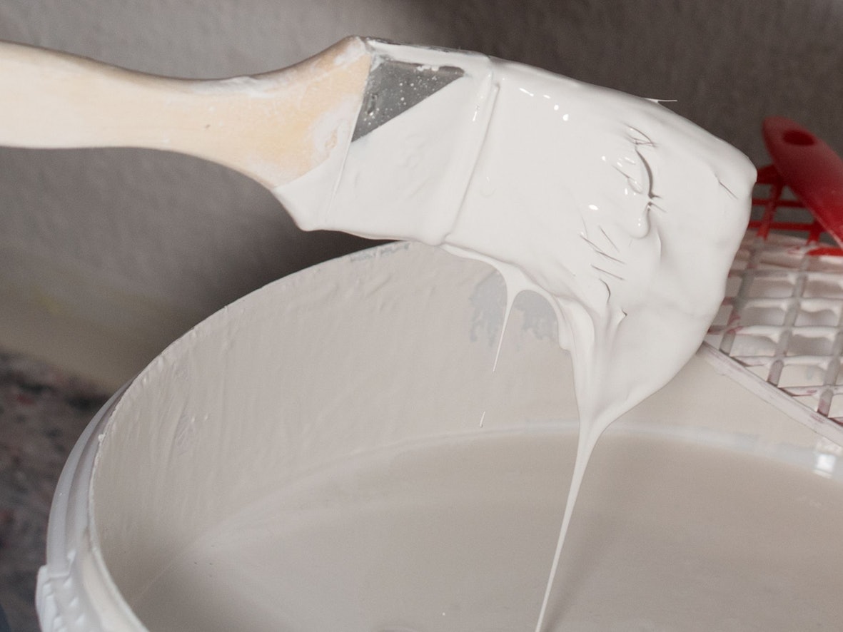 Ein Pinsel mit weißer Wandfarbe über einem Eimer.