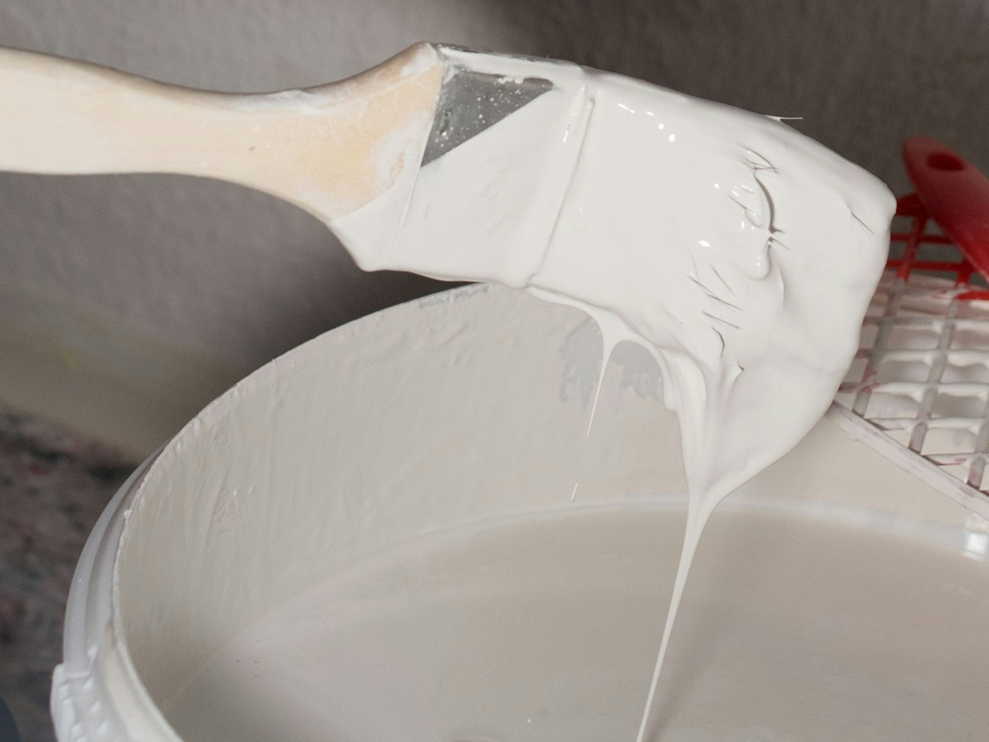 Ein Pinsel mit weißer Wandfarbe über einem Eimer.