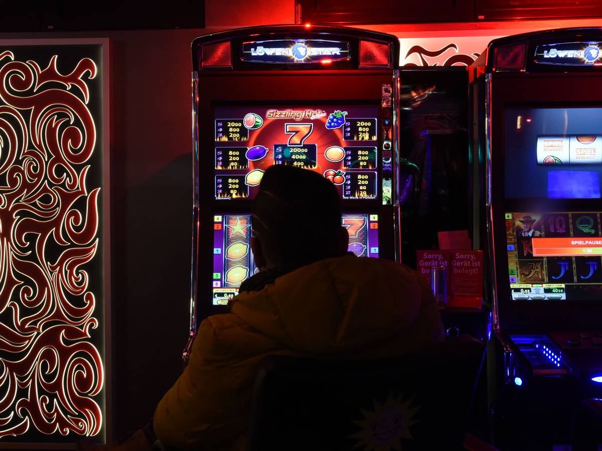 Mann sitzt in Spielhalle vor einem Automaten.