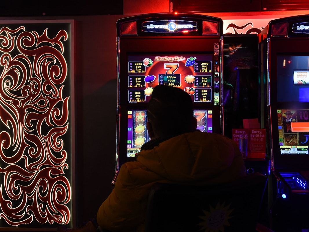 Mann sitzt in Spielhalle vor einem Automaten.