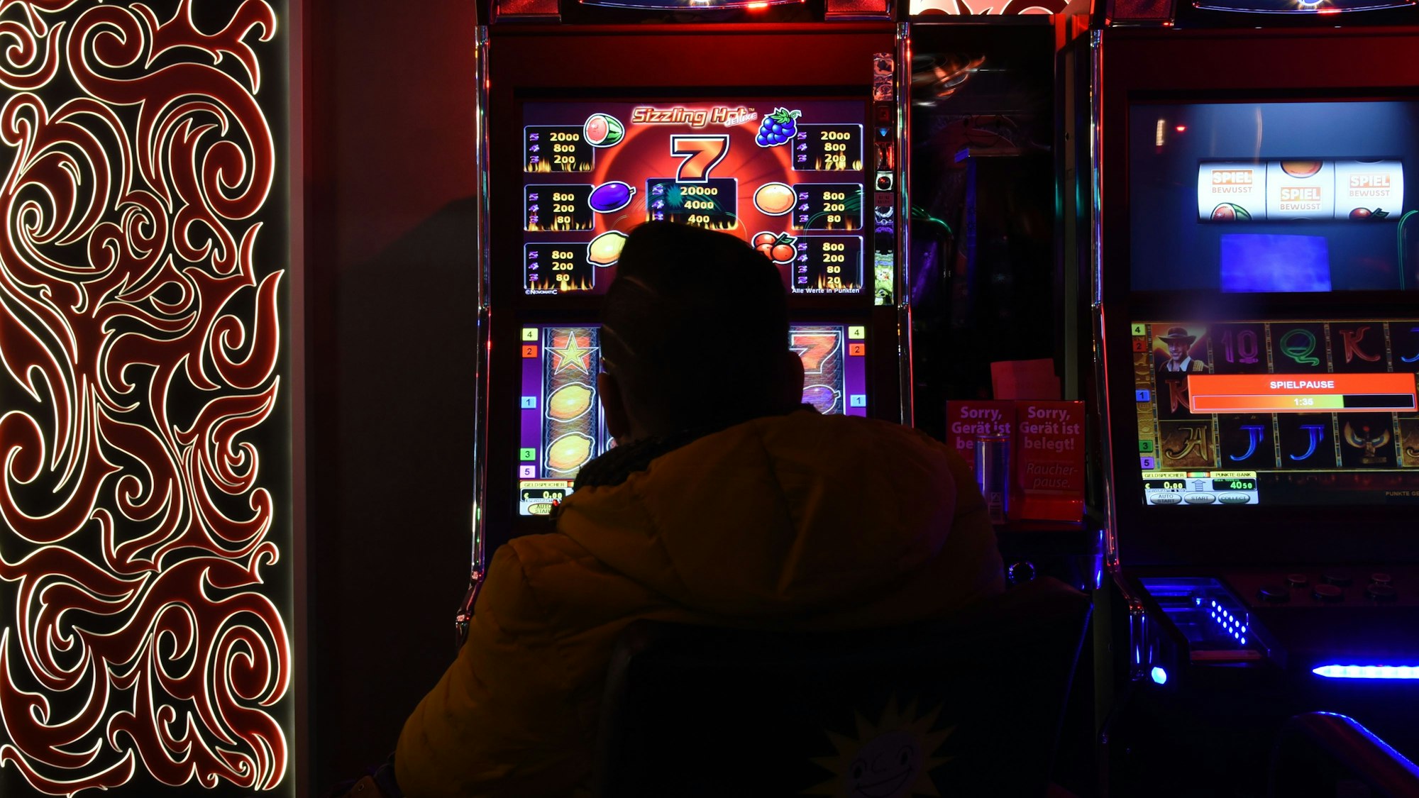 Mann sitzt in Spielhalle vor einem Automaten.