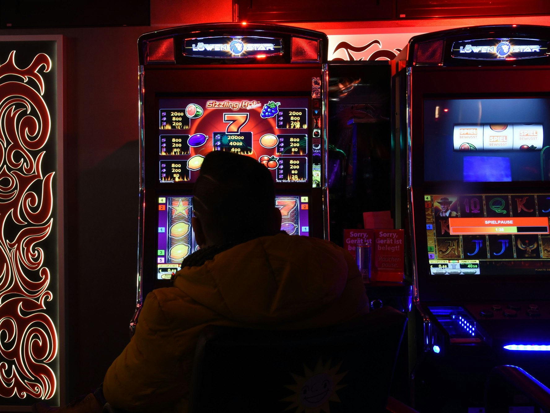 Mann sitzt in Spielhalle vor einem Automaten.