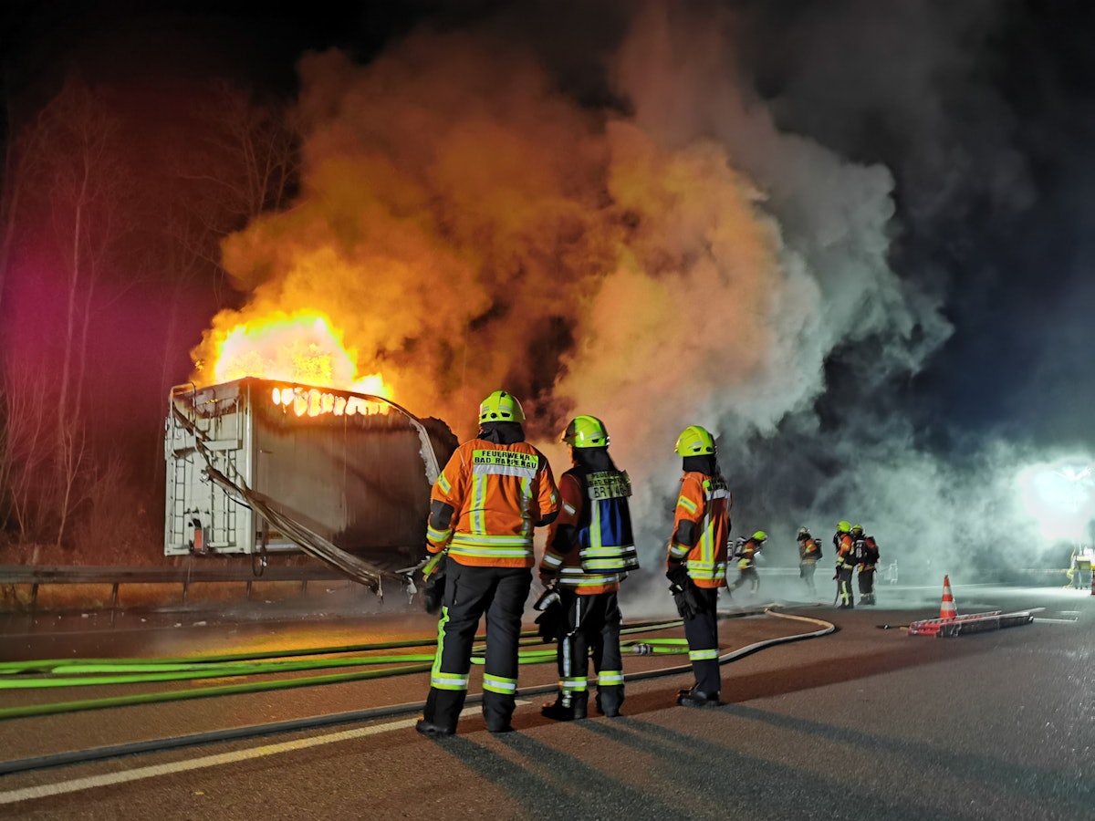 Feuerwehrleute vor einem brennenden Lkw auf der Autobahn.