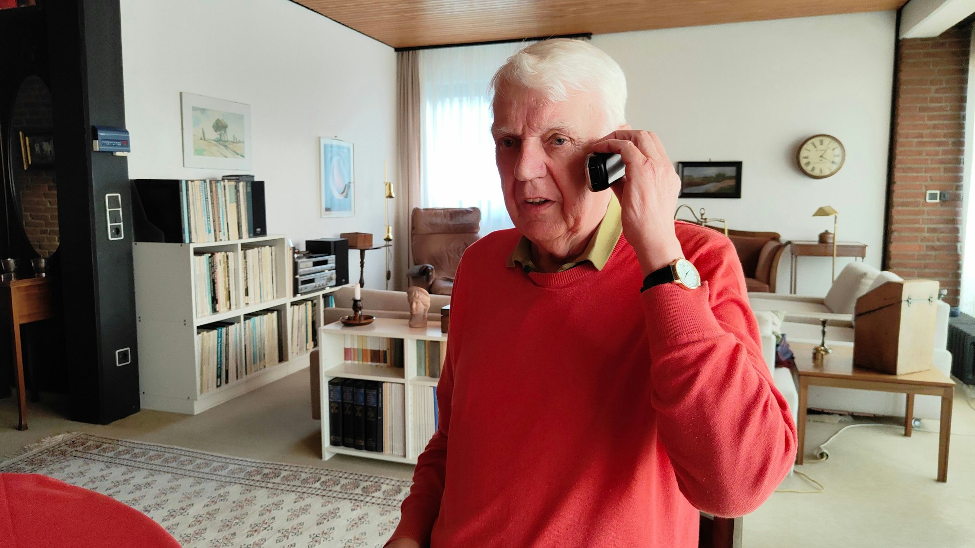 Rentner Herbert telefoniert in seinem Wohnzimmer.