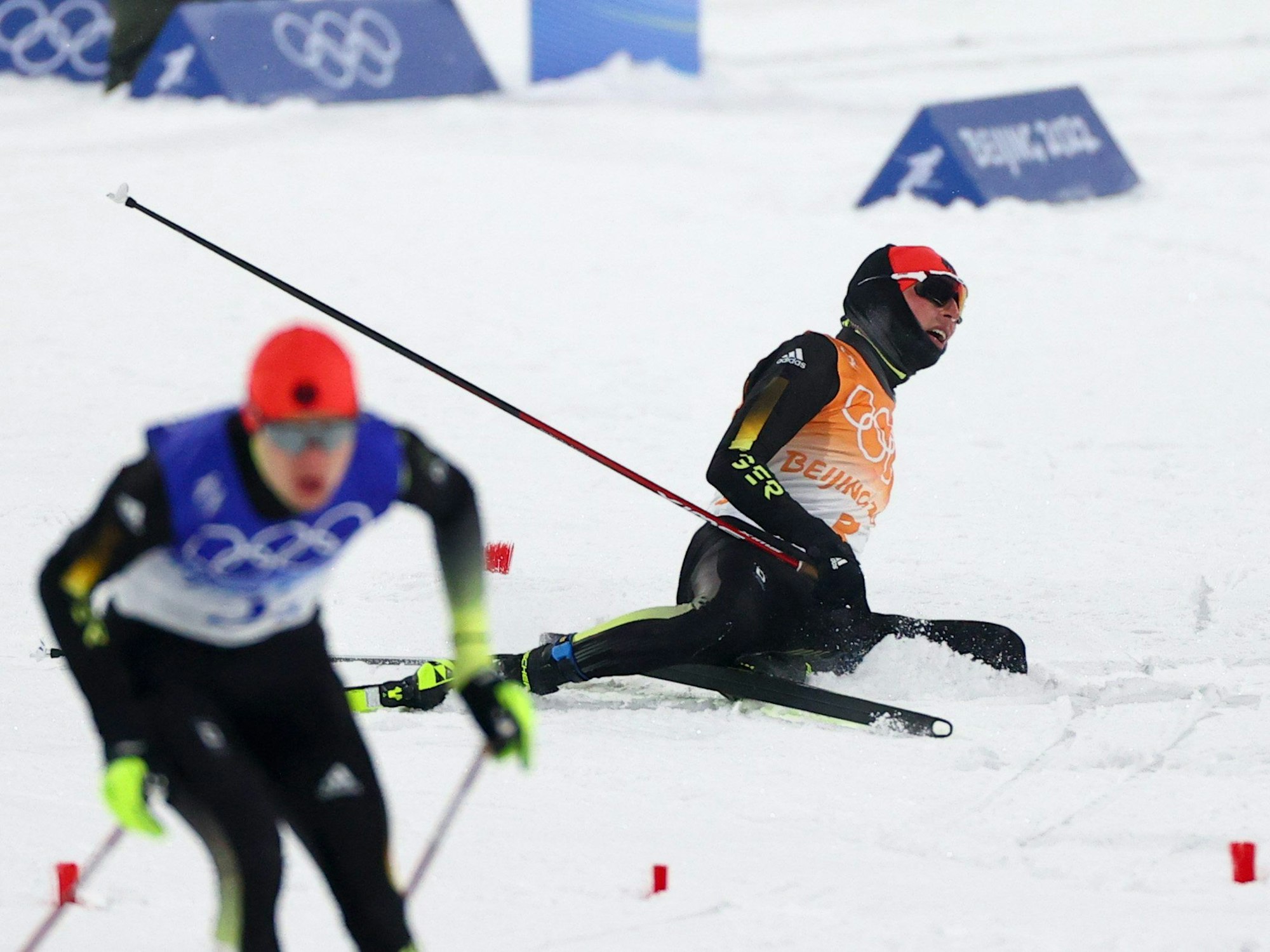 Eric Frenzel (r) aus Deutschland liegt nach dem Wechsel erschöpft auf dem Boden. Links läuft Vinzenz Geiger aus Deutschland.