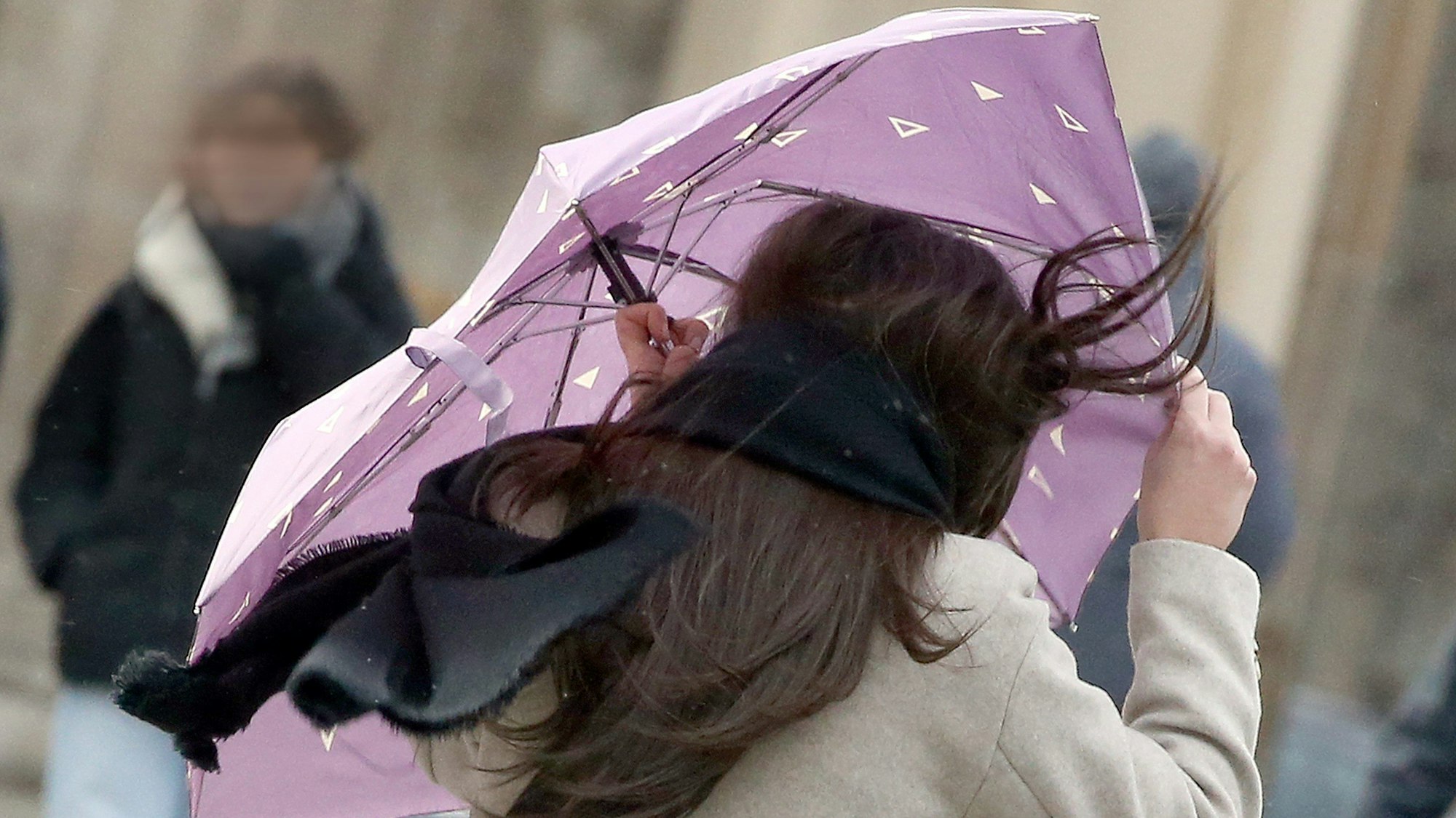 Eine Passantin mit wehenden Haaren sichert am Donnerstag (17. Februar) ihren Regenschirm, während sie sich bei Windstärken bis 100 km/h vor dem Brandenburger Tor entlang spaziert. Ein Experte erklärt, welchen Fehler die Deutschen auf keinen Fall machen sollten.