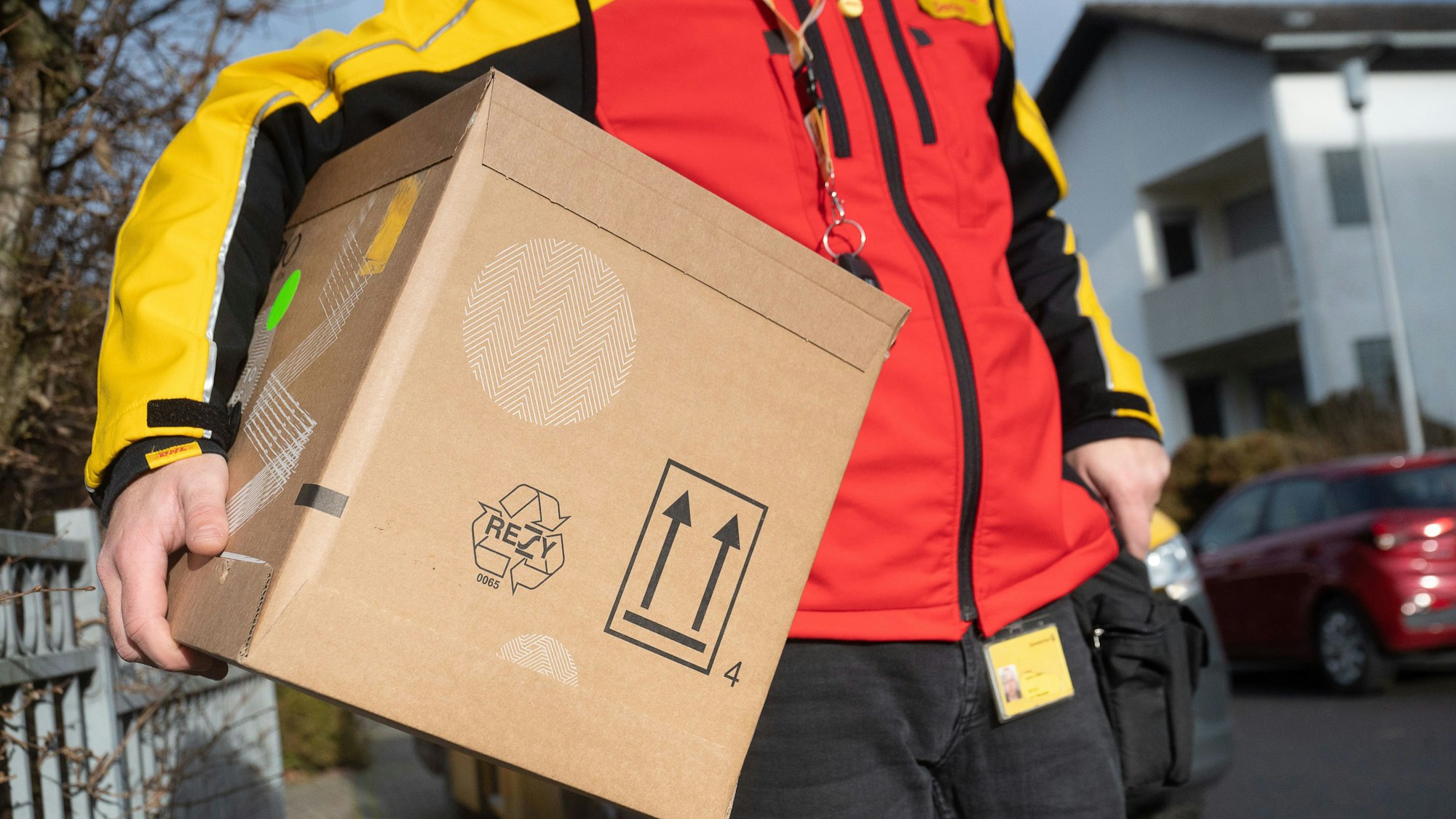 Ein DHL-Mitarbeiter trägt ein Paket unter seinem Arm.