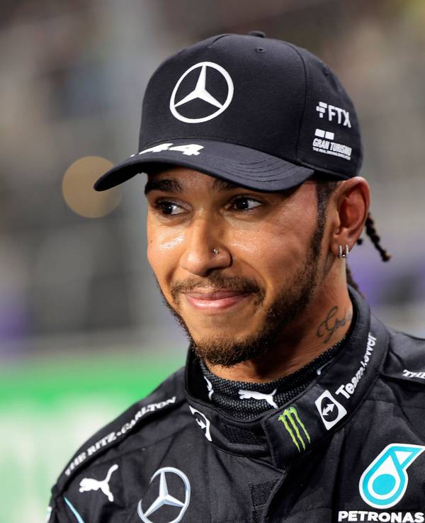Lewis Hamilton hat eine Kappe auf und lächelt.