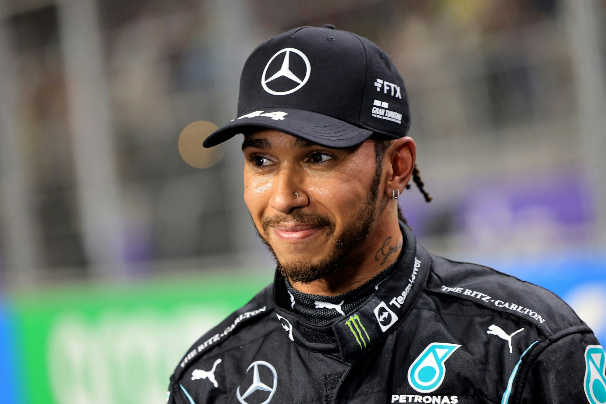 Lewis Hamilton hat eine Kappe auf und lächelt.