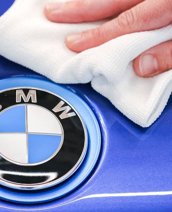 Ein Mitarbeiter von BMW poliert mit einem Tuch das Logo von einem BMW i8.