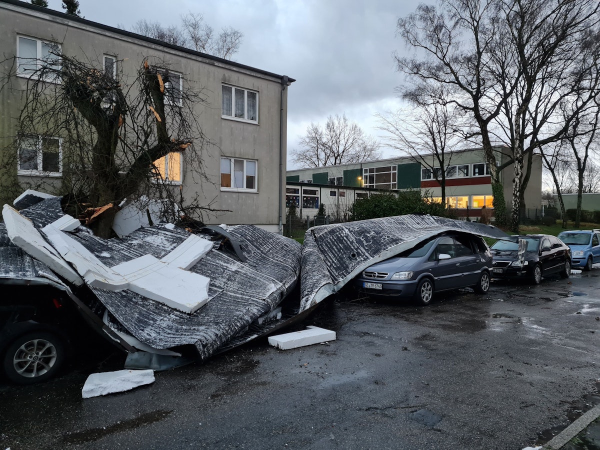 Teile eines vom Sturm Ylenia abgedeckten Flachdaches liegen auf einer Straße und auf geparkten Autos.