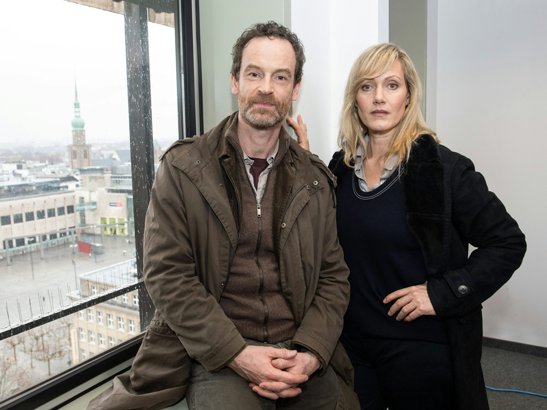 Die Schauspieler Jörg Hartmann, als Peter Faber, und Anna Schudt, als Martina Bönisch, stehen während der Dreharbeiten der ARD-Krimireihe „Tatort“ an einem Fenster mit Blick auf den Hansaplatz und die Reinoldikirche.