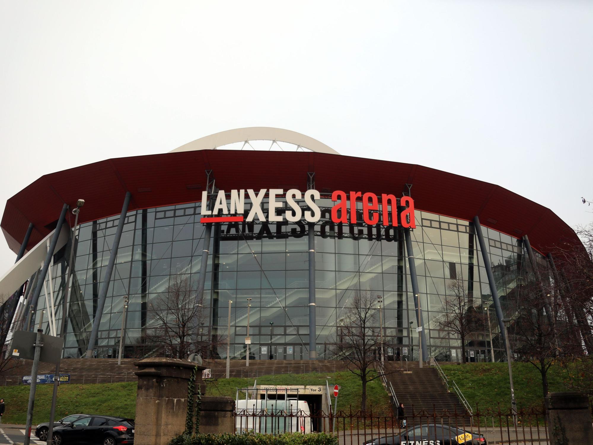 Die Lanxess Arena in Köln-Deutz mit fahrenden Autos im Vordergrund.