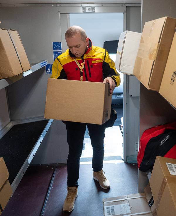 Ein DHL-Mitarbeiter sortiert in seinem Transporter Pakete für die nächsten Zustellungen.