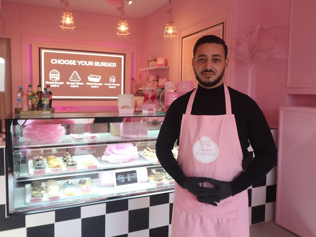 Ein Gastronom steht vor seinem Tresen mit Süßspeisen.