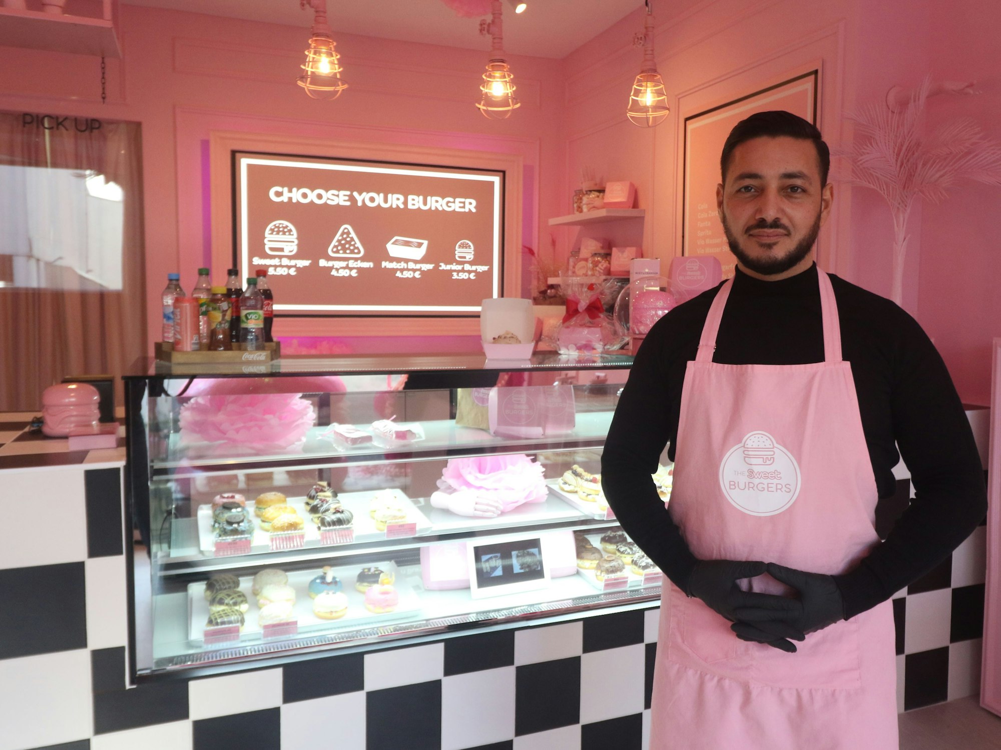 Ein Gastronom steht vor seinem Tresen mit Süßspeisen.