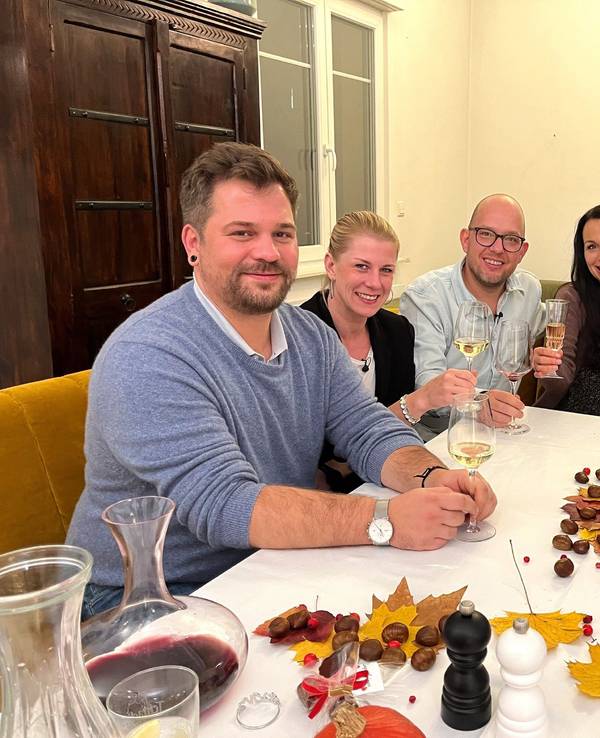 Die Das Perfekte Dinner-Kandidaten Marcus, Simone, Gastgeber Andreas, Sabrina und Jürgen sitzen an Andreas Tisch und lächeln.