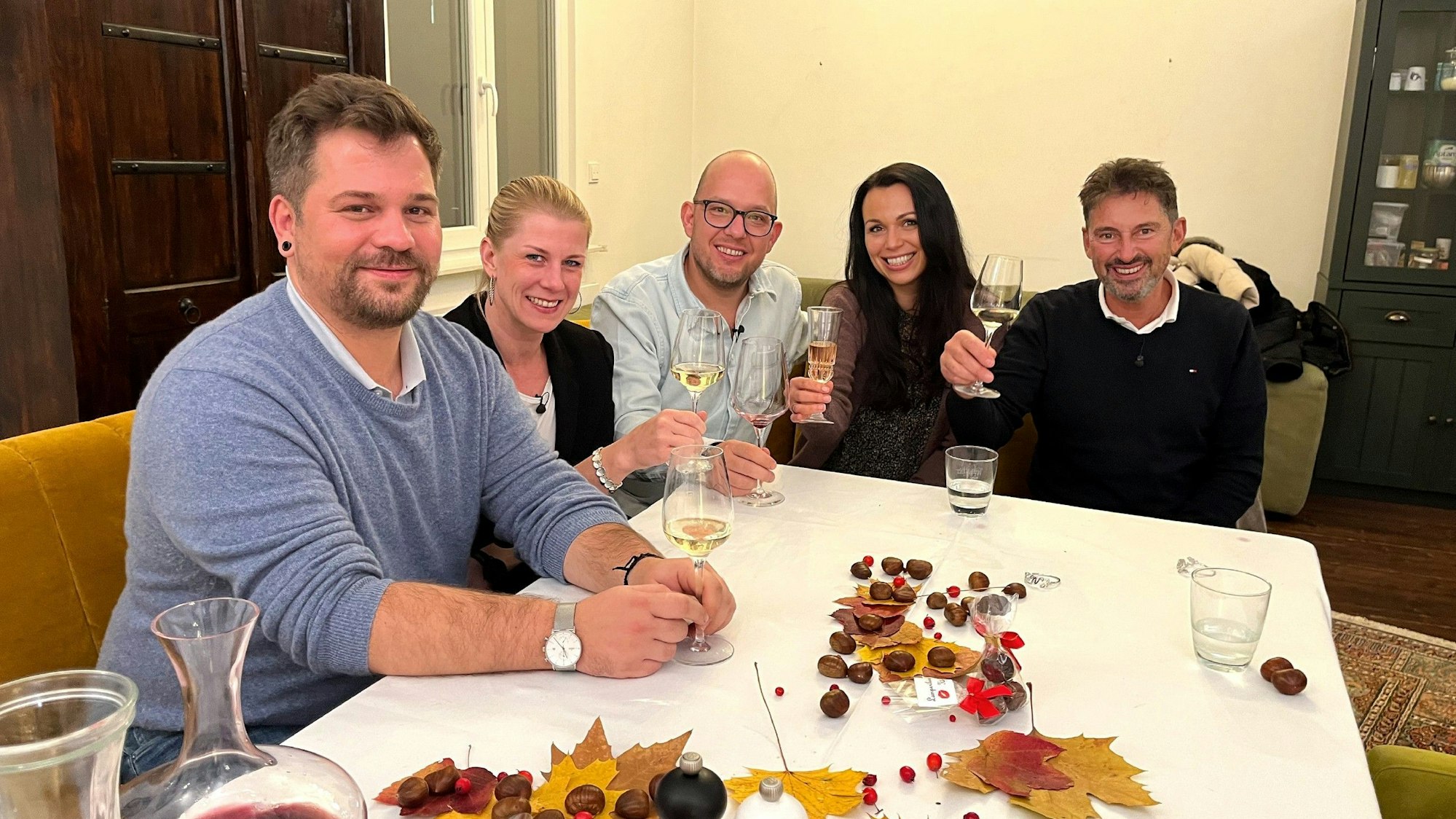 Die Das Perfekte Dinner-Kandidaten Marcus, Simone, Gastgeber Andreas, Sabrina und Jürgen sitzen an Andreas Tisch und lächeln.