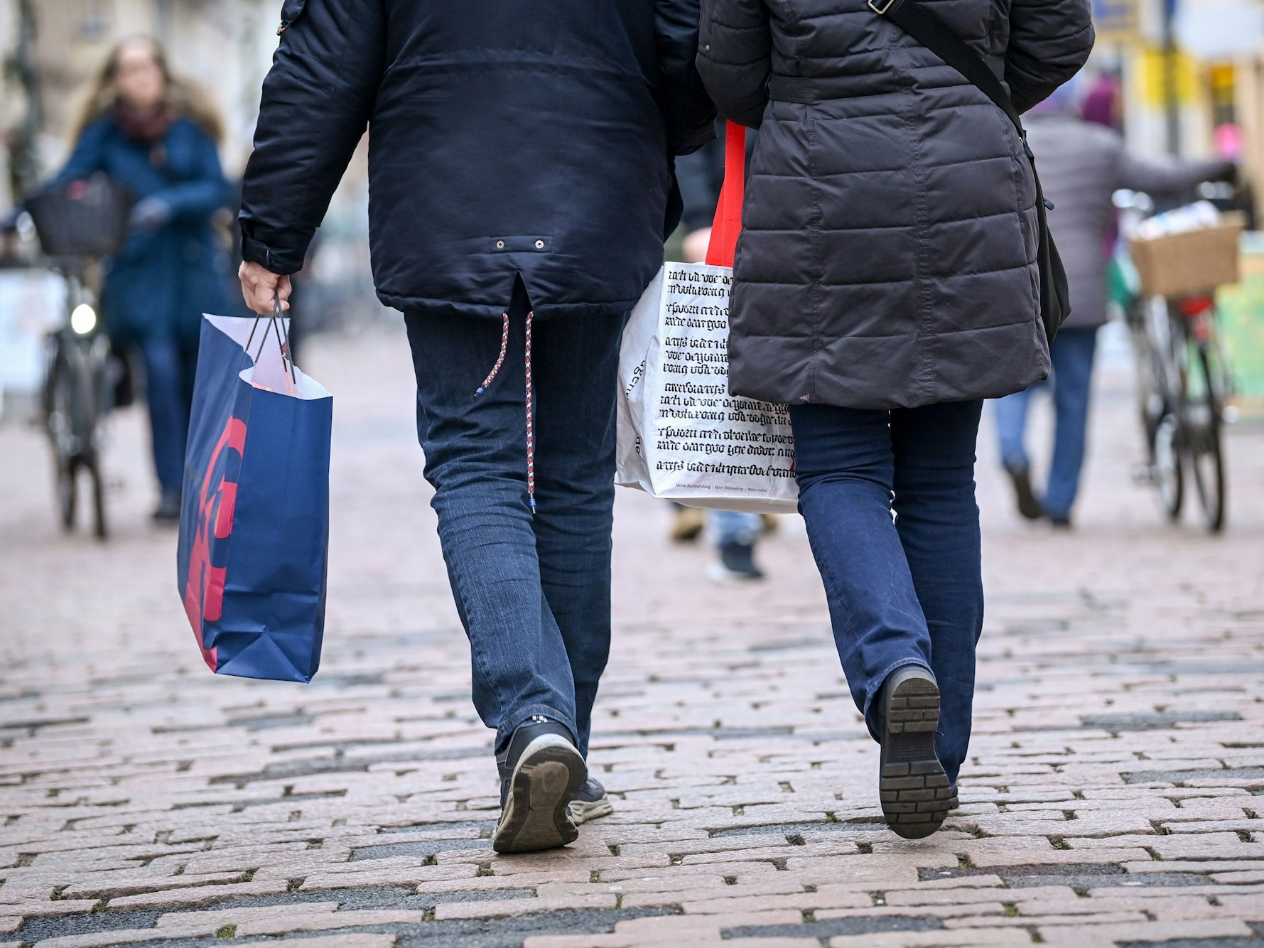 Das undatierte Symbolfoto zeigt zwei Personen von hinten. Sie gehen eine Straße entlang, beide haben eine Einkaufstüte in der Hand.