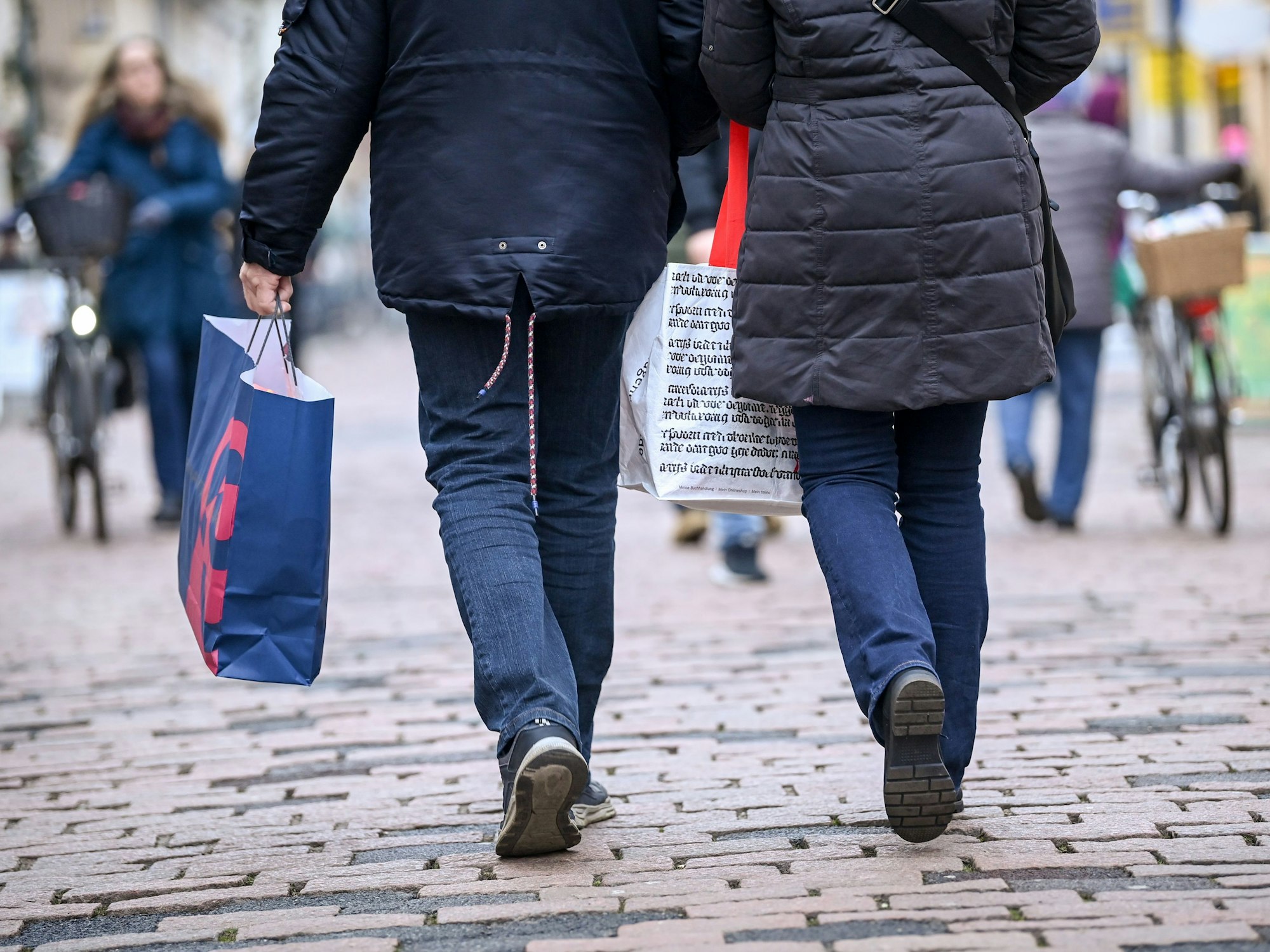 Das undatierte Symbolfoto zeigt zwei Personen von hinten. Sie gehen eine Straße entlang, beide haben eine Einkaufstüte in der Hand.