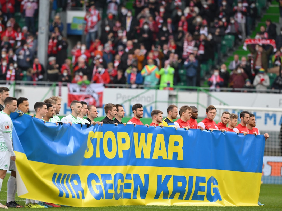 Die Spieler von Greuther Fürth und dem 1. FC Köln halten ein Banner hoch.