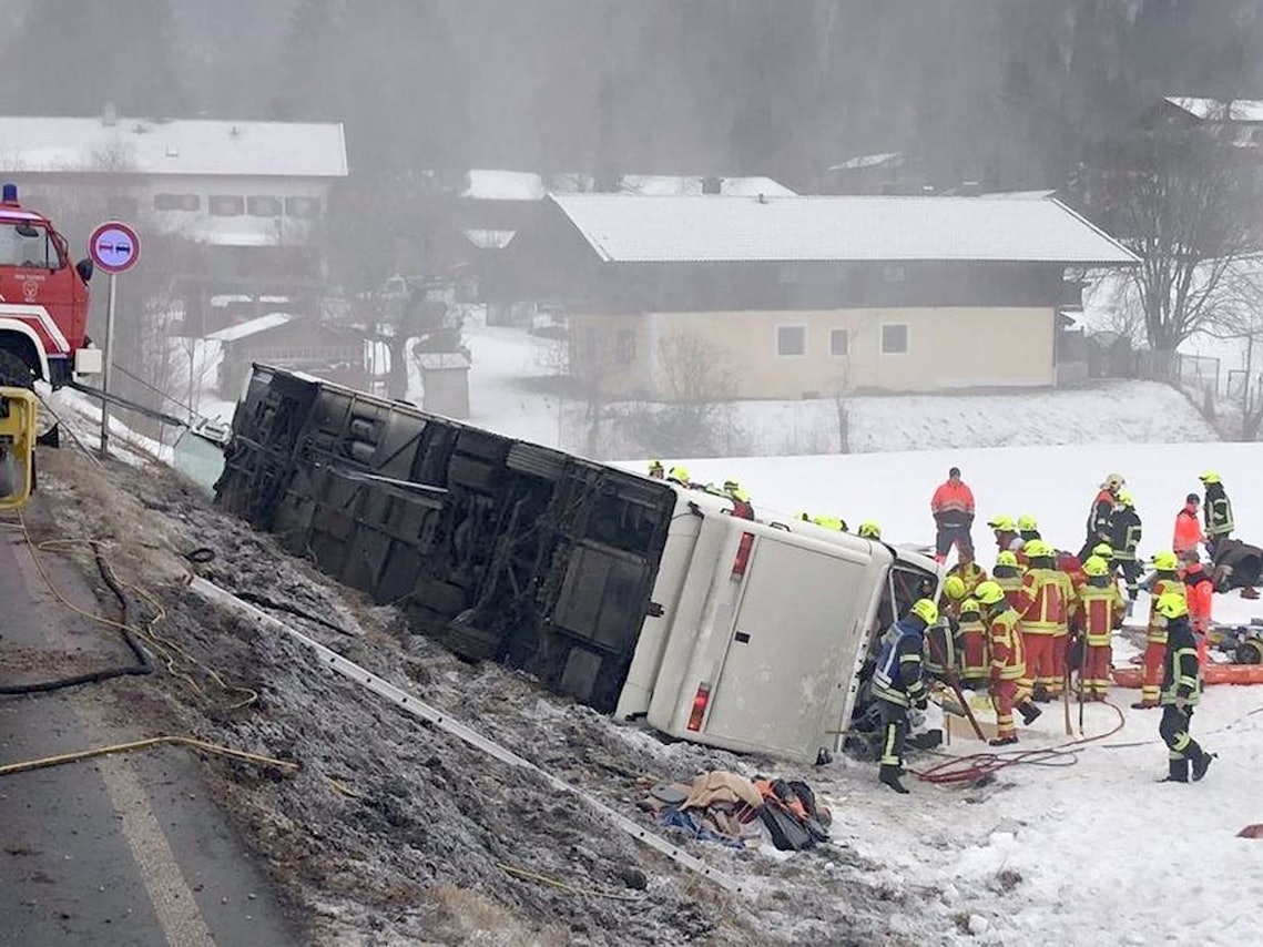 Einsatzkräfte der Feuerwehr stehen auf der Bundesstraße B306 am Ortsausgang von Inzell (Landkreis Traunstein) neben einem umgekippten Reisebus am Straßenrand.