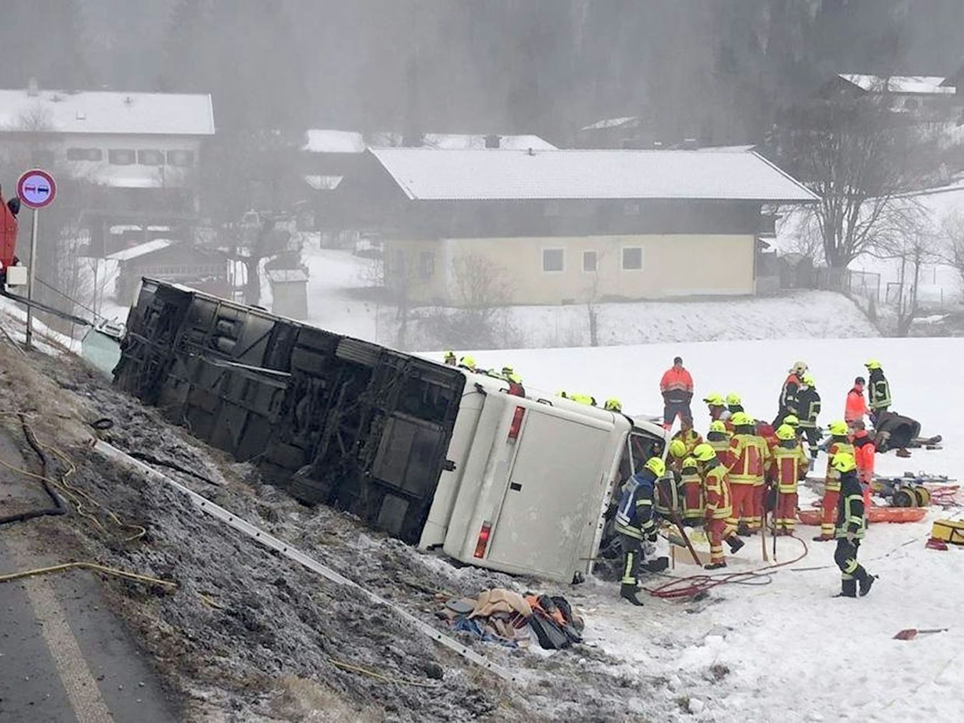Einsatzkräfte der Feuerwehr stehen auf der Bundesstraße B306 am Ortsausgang von Inzell (Landkreis Traunstein) neben einem umgekippten Reisebus am Straßenrand.